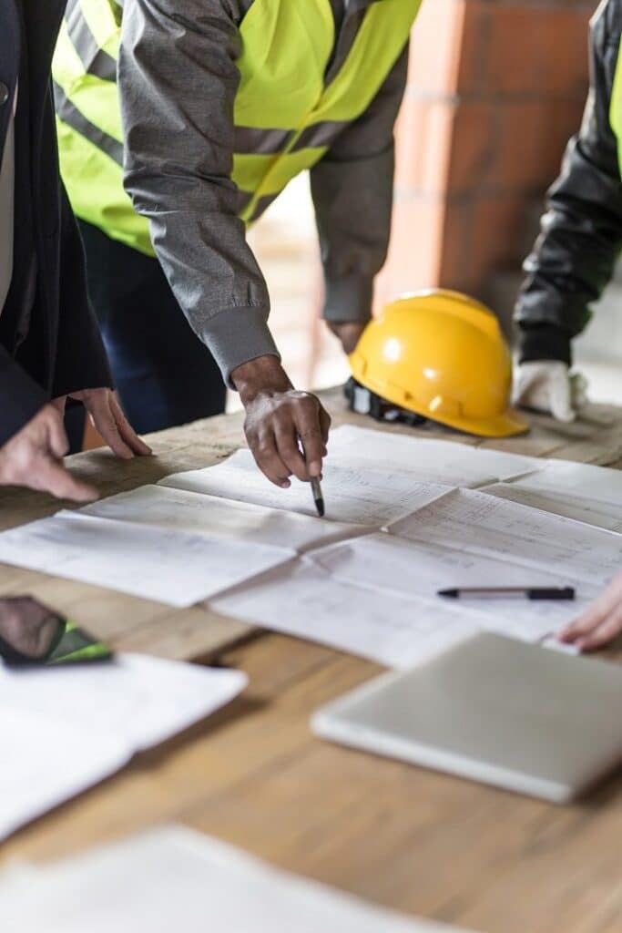 Construction worker Construction team reviewing blueprints on site, wearing high-visibility vests and hard hats, planning project details. | Sky Rye Design Construction team reviewing blueprints on site, wearing high-visibility vests and hard hats, planning project details.