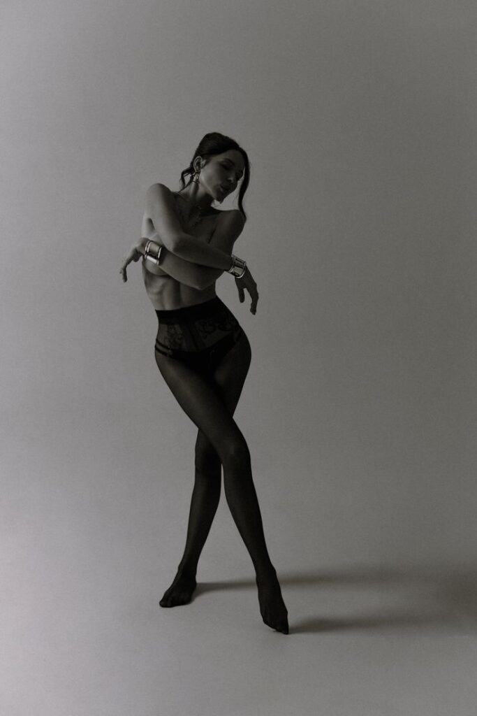 Artistic black and white photo of a woman in stylish sheer attire striking an elegant pose.