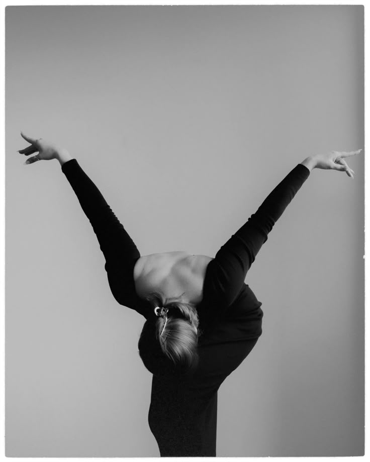 Elegant dancer in black, gracefully arching back with arms extended, captured in a dynamic, monochromatic pose.