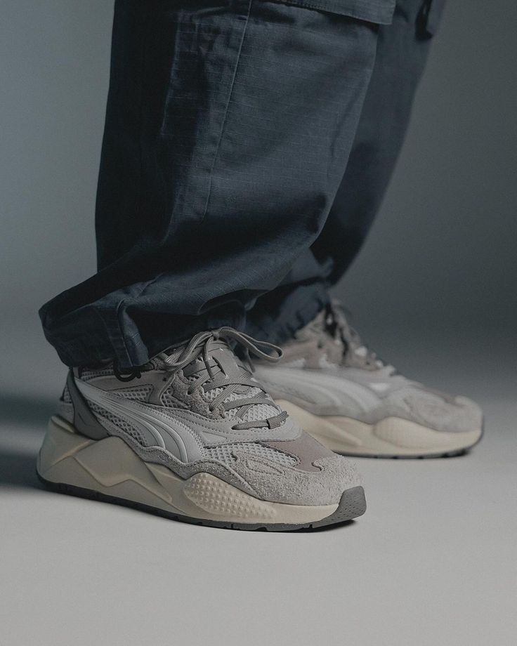 Gray sneakers paired with dark pants, showcasing modern casual footwear style in a minimalistic setting.