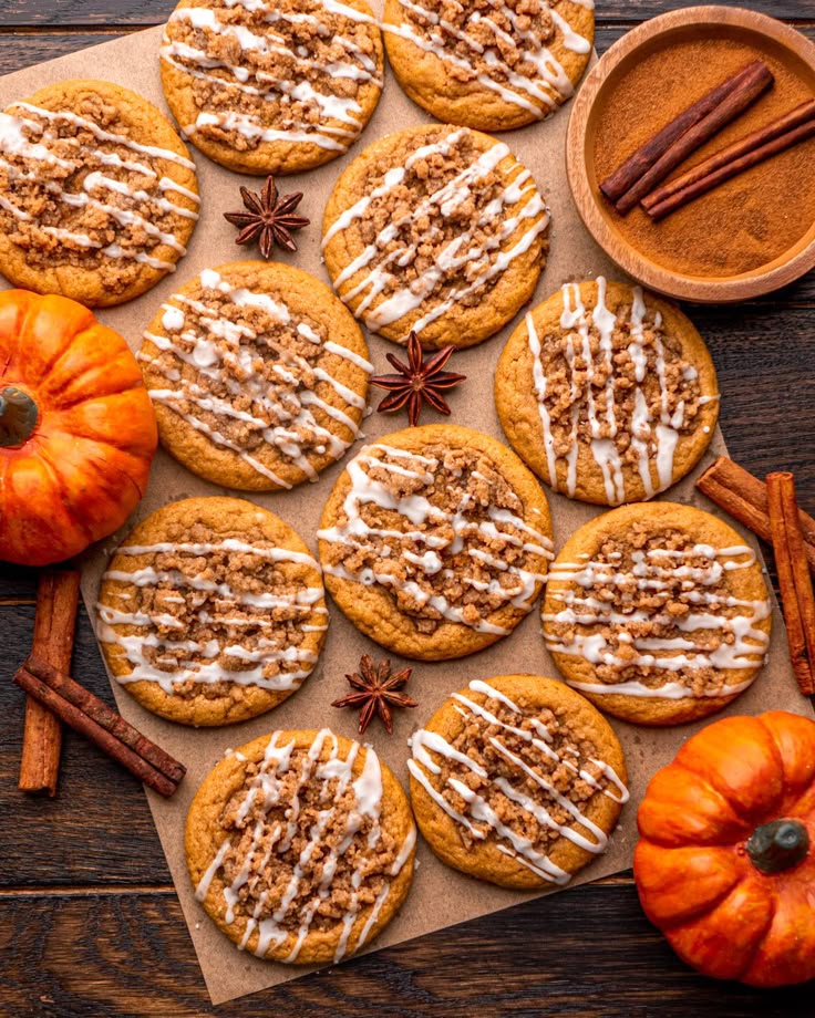 Pumpkin cookies with icing and crumble topping, surrounded by pumpkins, cinnamon sticks, and star anise on a wooden table.