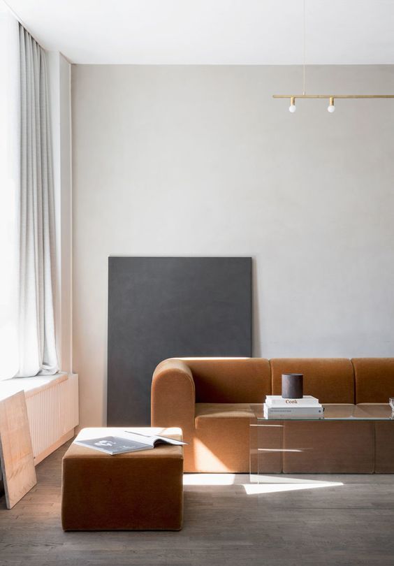 Minimalist living room with a brown sofa, glass coffee table, and abstract art against a light gray wall.