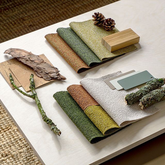 Fabric swatches in earthy tones with natural textures, pinecones, and wood samples on a light tabletop.