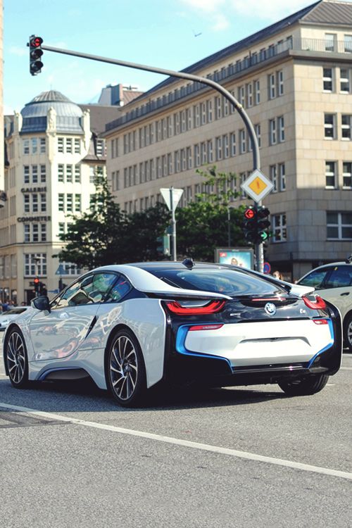 Futuristic sports car driving through city intersection with historic buildings in background.