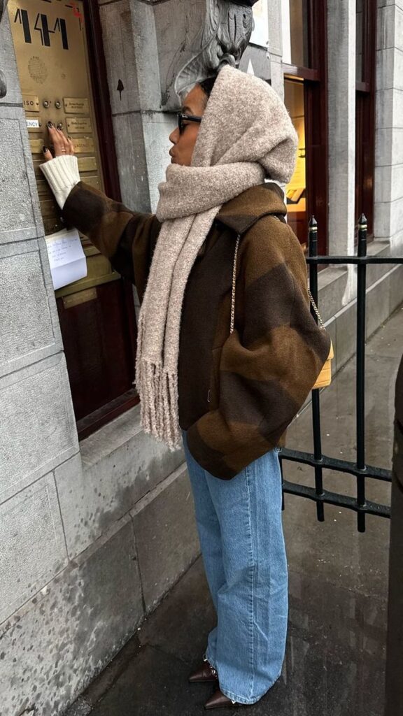 Woman in cozy scarf and jacket presses a button on a door panel outdoors.