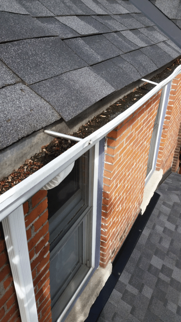 Roof gutter filled with leaves and debris on a brick building, needing cleaning for proper drainage.