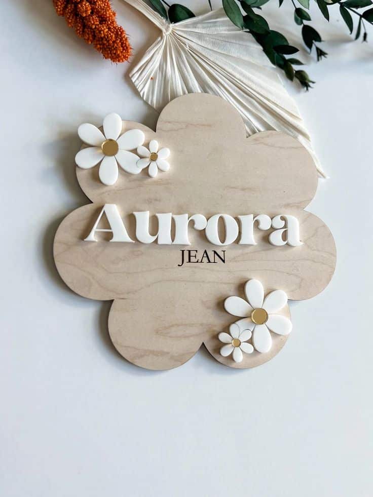 Wooden floral name sign Aurora Jean with white daisies and decorative leaves.