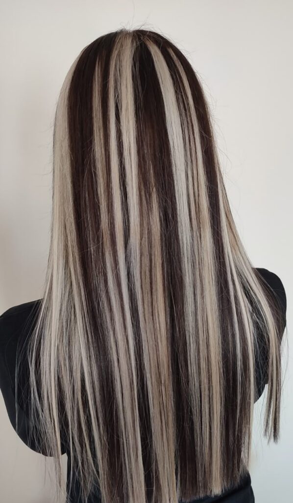 Long straight hair with black and blonde highlights, showcasing a modern hairstyle against a neutral background.
