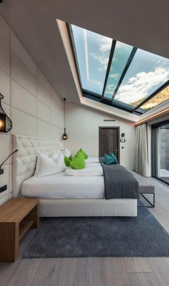 Modern bedroom with skylight, stylish decor, green pillows, and a cozy ambiance.