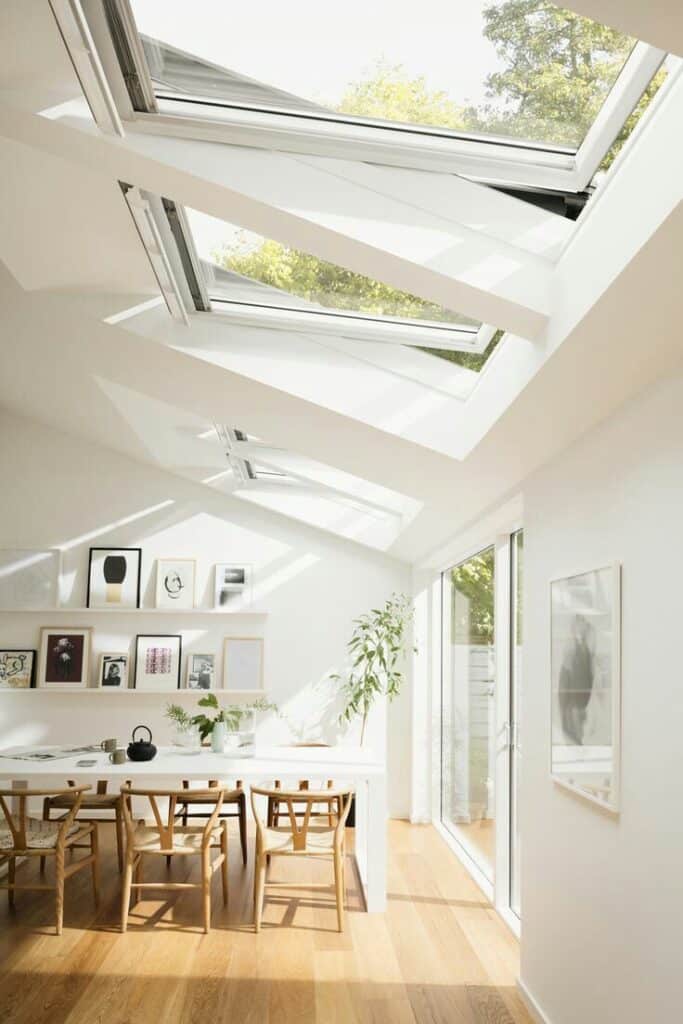 Modern dining room with skylights, wooden chairs, and plants, creating a bright, airy ambiance.