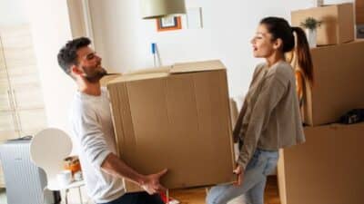 Couple moving a large cardboard box in a bright room, preparing for relocation.