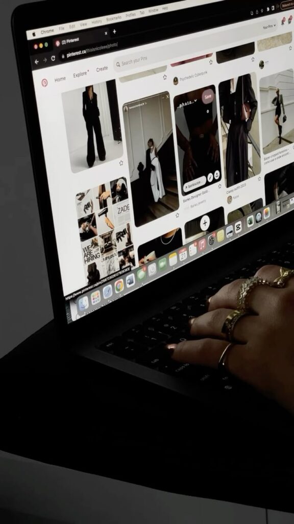 Person browsing fashion photos on Pinterest using a laptop in a dimly lit setting.