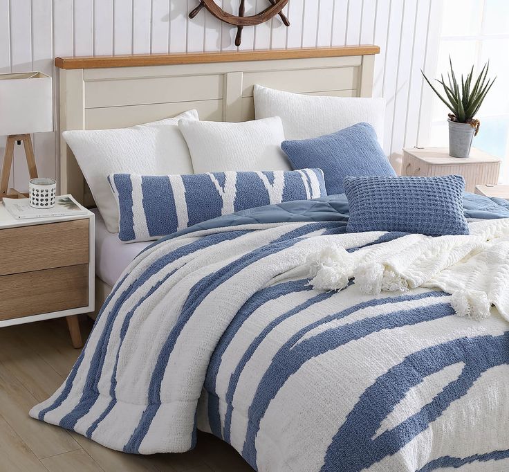 Cozy bedroom with blue and white striped bedding, white pillows, and a wooden bedside table with decor.