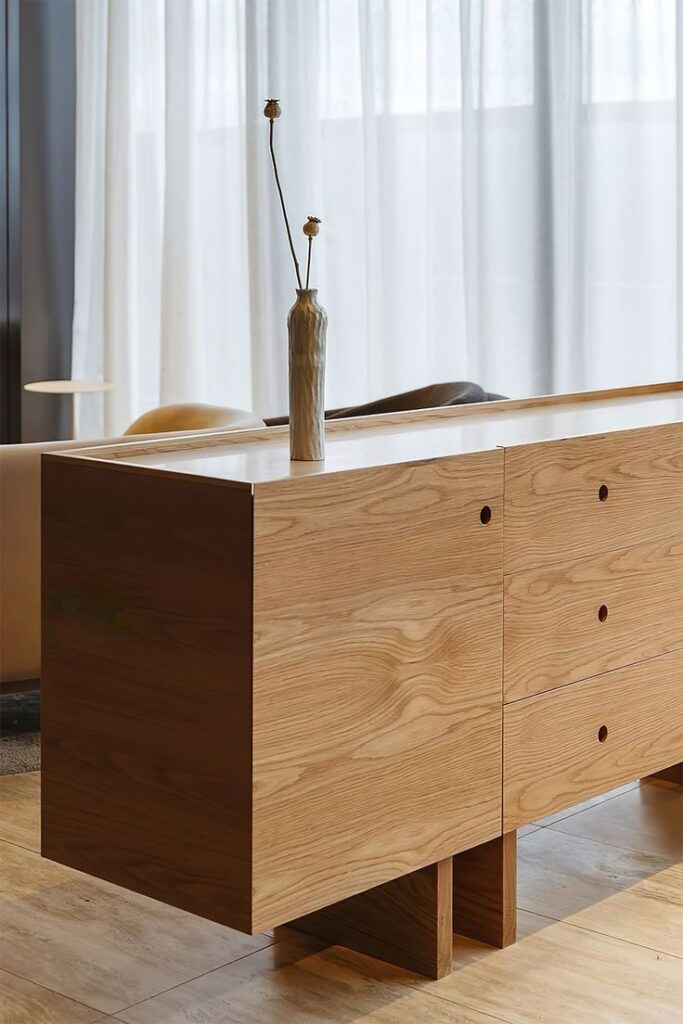 Minimalist wooden sideboard with a tall vase, enhancing the modern interior design with sheer curtains in the background.