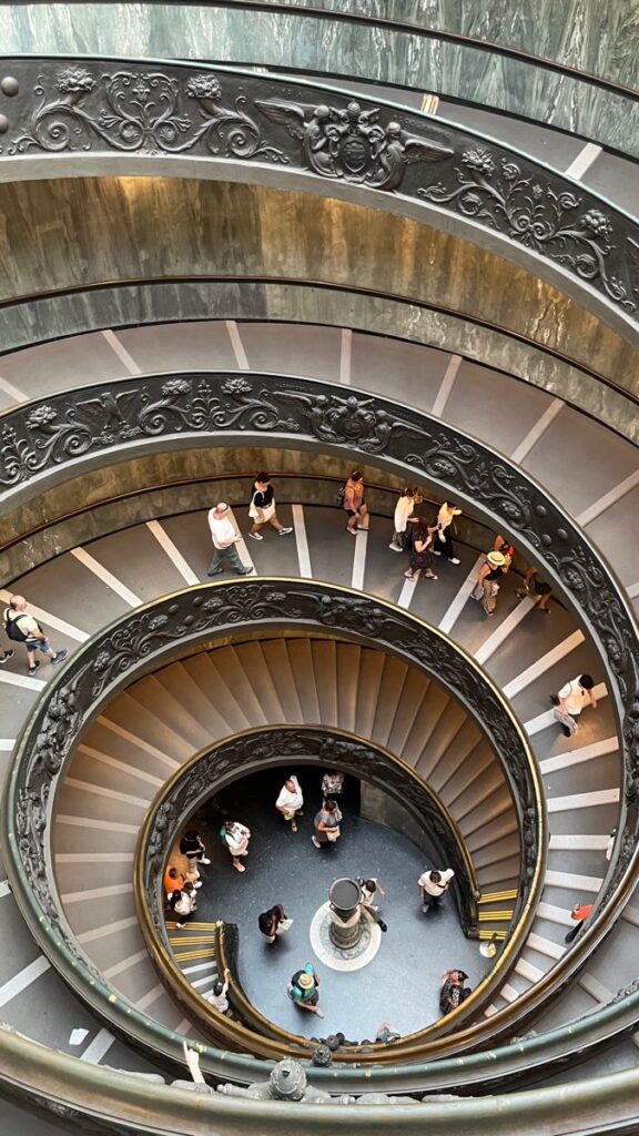 Aerial view of a spiral staircase with ornate railings and people walking, showcasing architectural beauty.