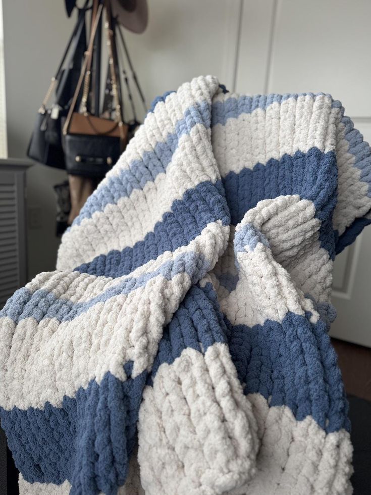 Cozy blue and white striped knit blanket draped over a chair with handbags in the background.
