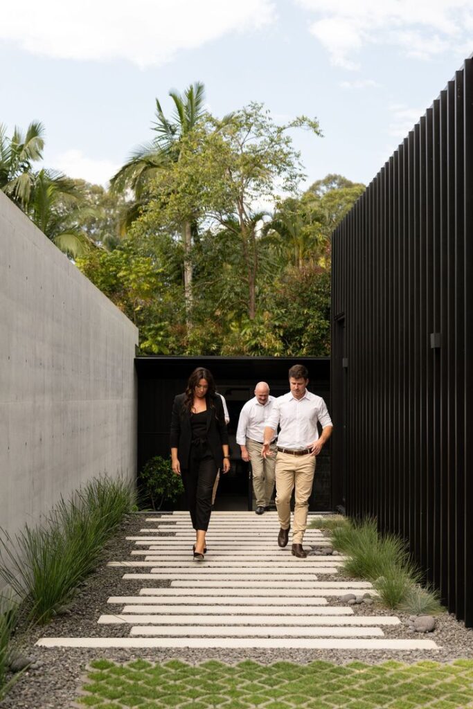 Group of professionals walking on a modern outdoor walkway surrounded by greenery and sleek architecture.