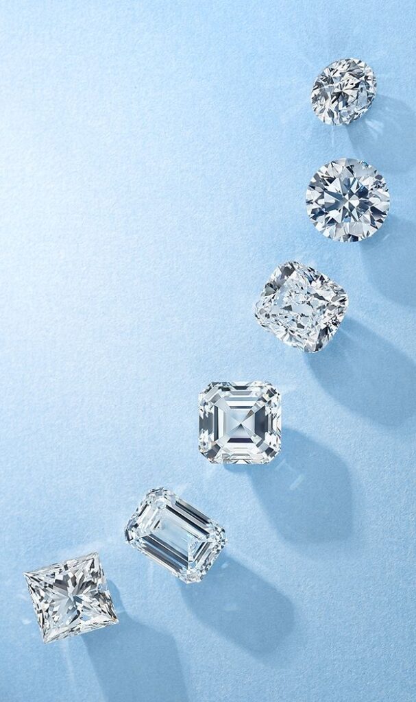 Assorted diamond cuts on blue background, showcasing round, princess, and emerald shapes.