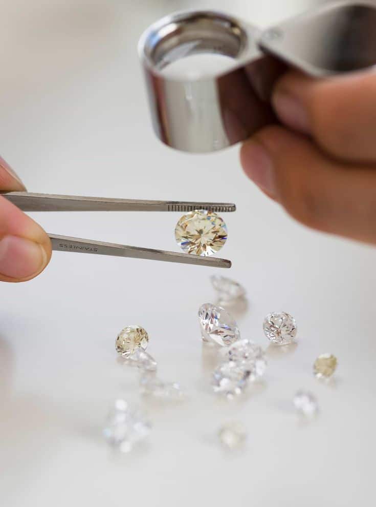 Gemologist inspecting diamonds with tweezers and loupe on white surface.