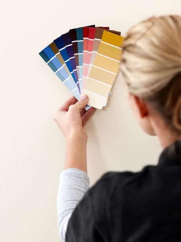 Person holding color swatches against a wall, exploring paint options for interior design and decoration.