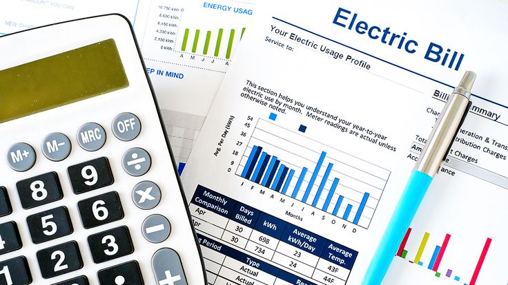 Calculator and pen on electric bill statement with charts and graphs showing energy usage analysis.