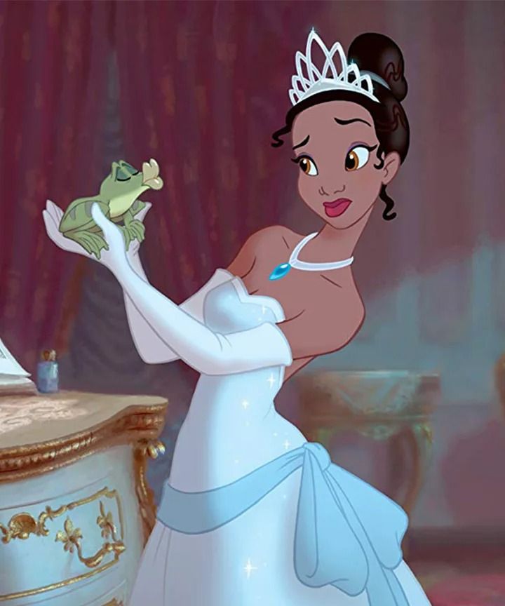 Princess in a blue gown holds a frog, wearing a tiara and gloves, in an elegant room setting.