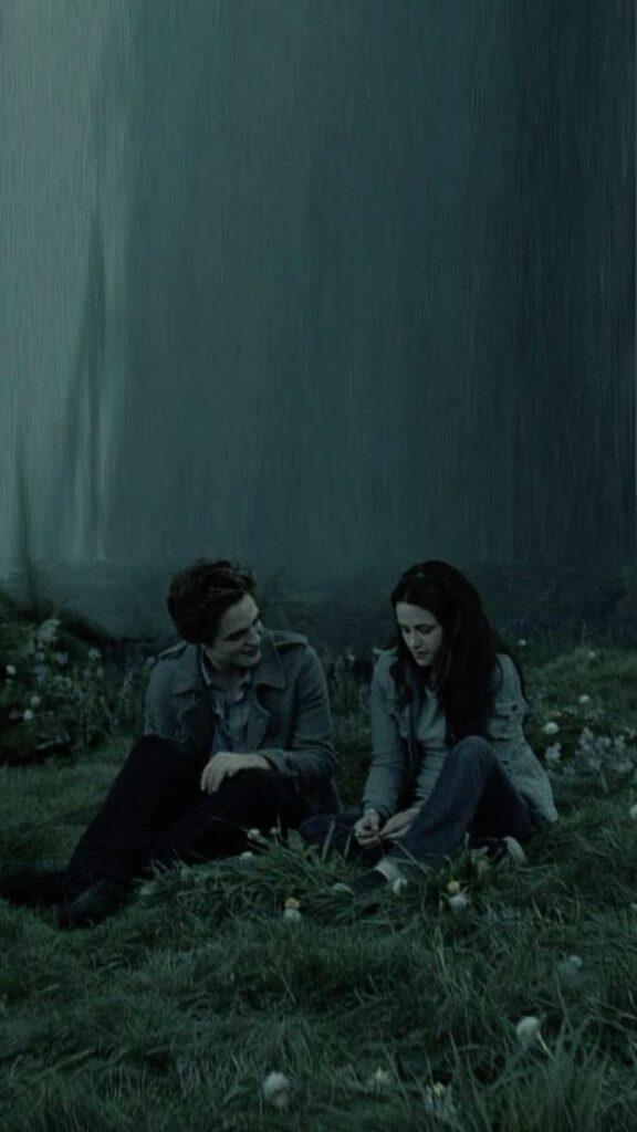 Two people sitting on grass, talking intimately in a dark, forested setting.