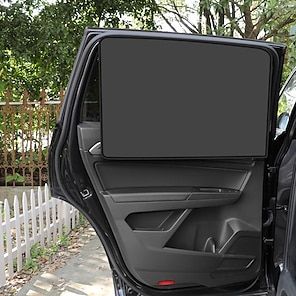 Car rear door open with sunshade installed, parked by white fence under trees.