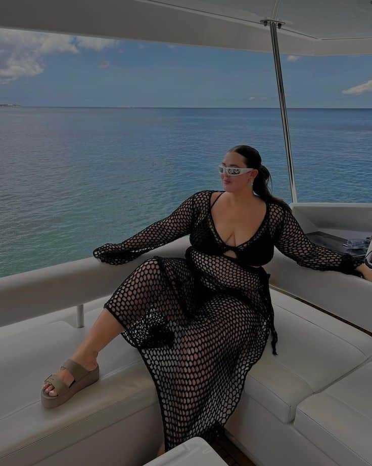 Woman in a stylish black mesh cover-up relaxing on a yacht, enjoying a sunny day at sea.