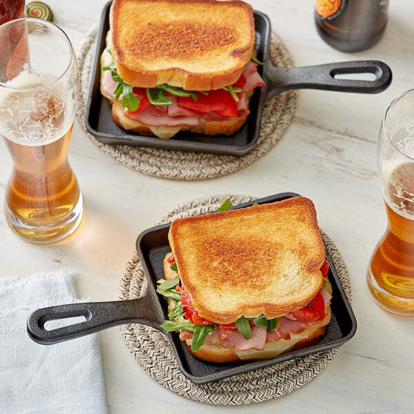 Grilled ham and cheese sandwiches with arugula in mini pans, served with glasses of beer on a white table.