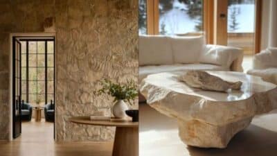 Modern living room with stone walls, rustic decor, large windows, and natural light on a stone coffee table.