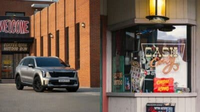 Silver SUV parked near a brick building with a Welcome sign and a Cash Only tattoo parlor window display.