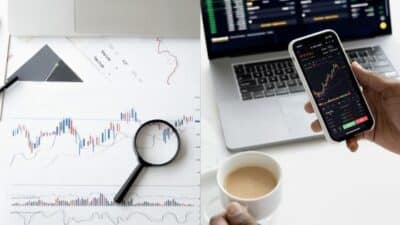 Stock market analysis with charts on paper and a smartphone, magnifying glass and laptop.
