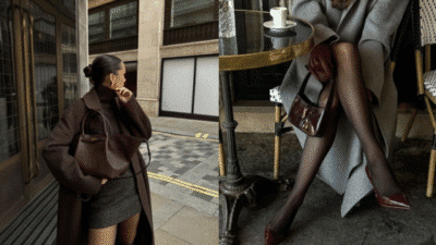 Stylish woman in a brown coat and handbag, sitting at a café table with crossed legs, showcasing chic fashion.