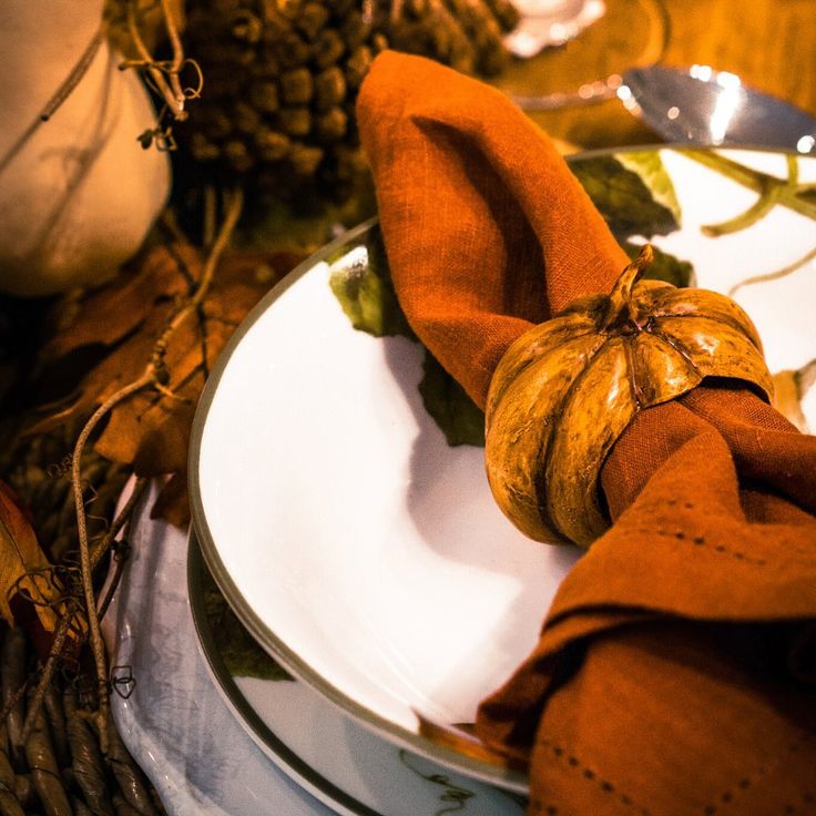 Festive autumn table setting with orange napkin and pumpkin decor on a white plate, surrounded by fall leaves.