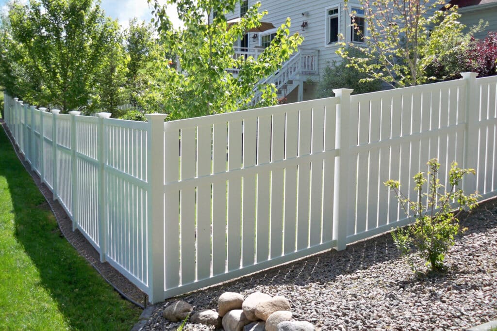 White vinyl fence bordering a garden with trees and gravel, enhancing backyard privacy and landscaping.