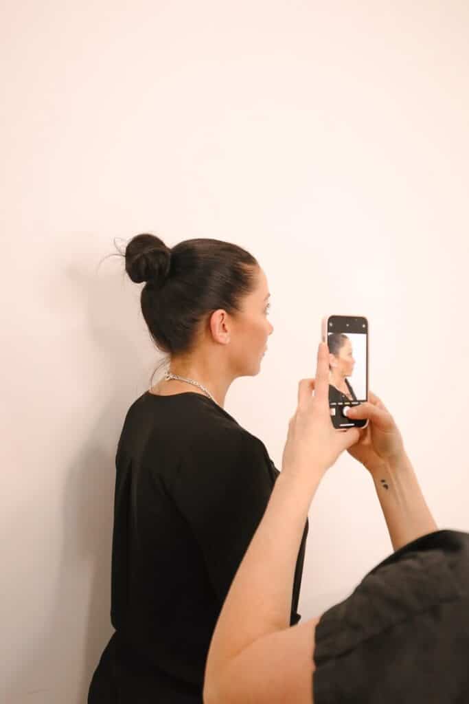 Person with bun hairstyle photographed with smartphone against beige background.