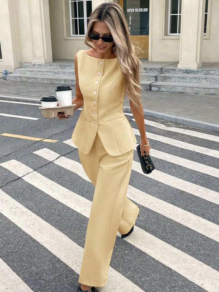 Stylish woman in a yellow suit crossing a street carrying coffee and a handbag, showcasing urban fashion.