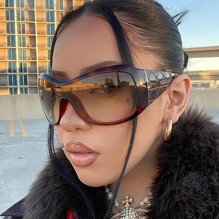 Fashionable woman wearing oversized sunglasses and gold hoop earrings in urban setting.