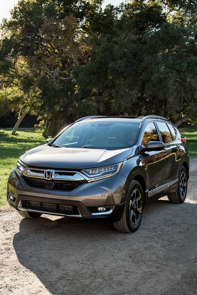 Grey Honda CR-V SUV parked on a sunny dirt road with trees in the background.