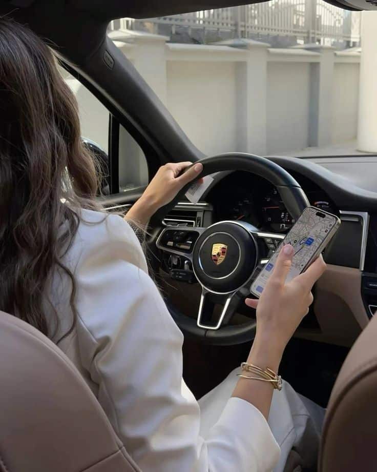 Woman using GPS on phone while driving a Porsche, showcasing modern technology and luxury lifestyle.