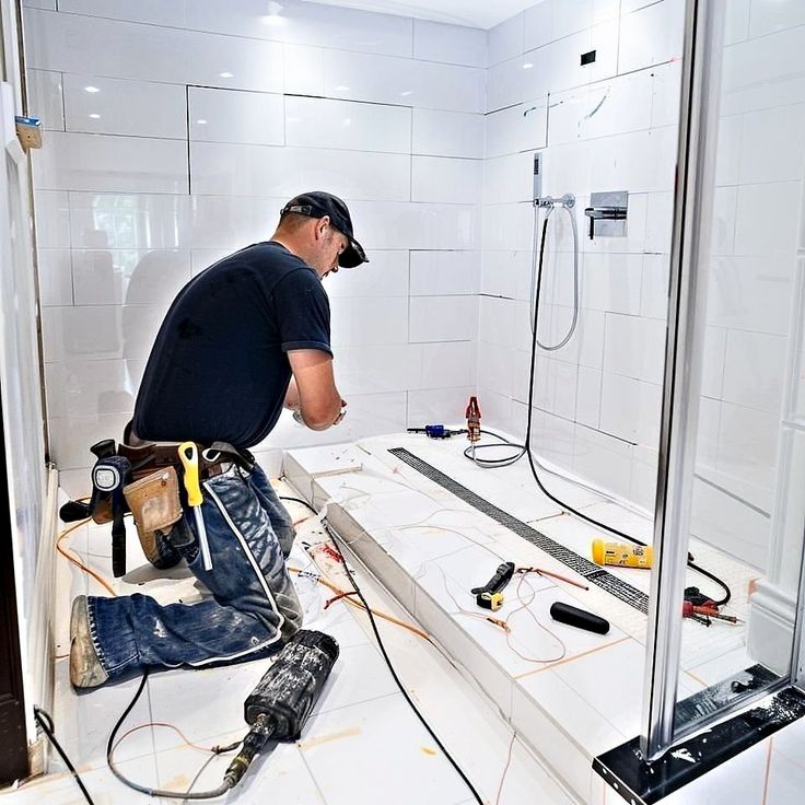 Construction worker tiling a modern bathroom floor with tools scattered around.