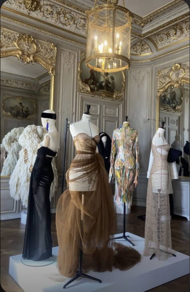 Luxurious fashion display with elegant gowns on mannequins in an ornate, vintage room.
