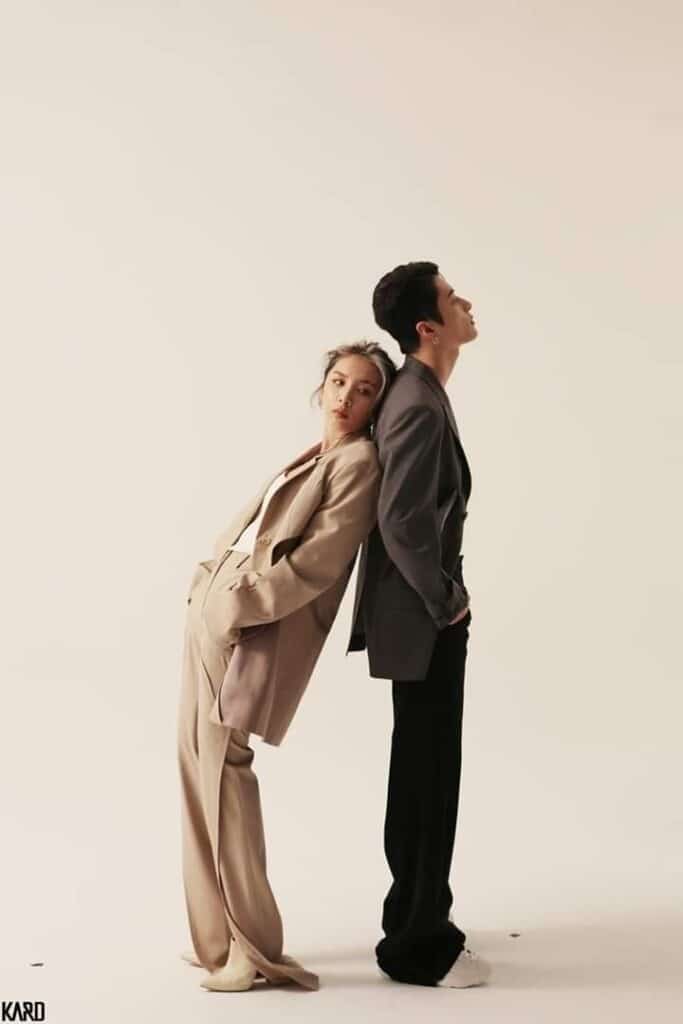 Two fashionable individuals in stylish suits, leaning back-to-back against a neutral background.