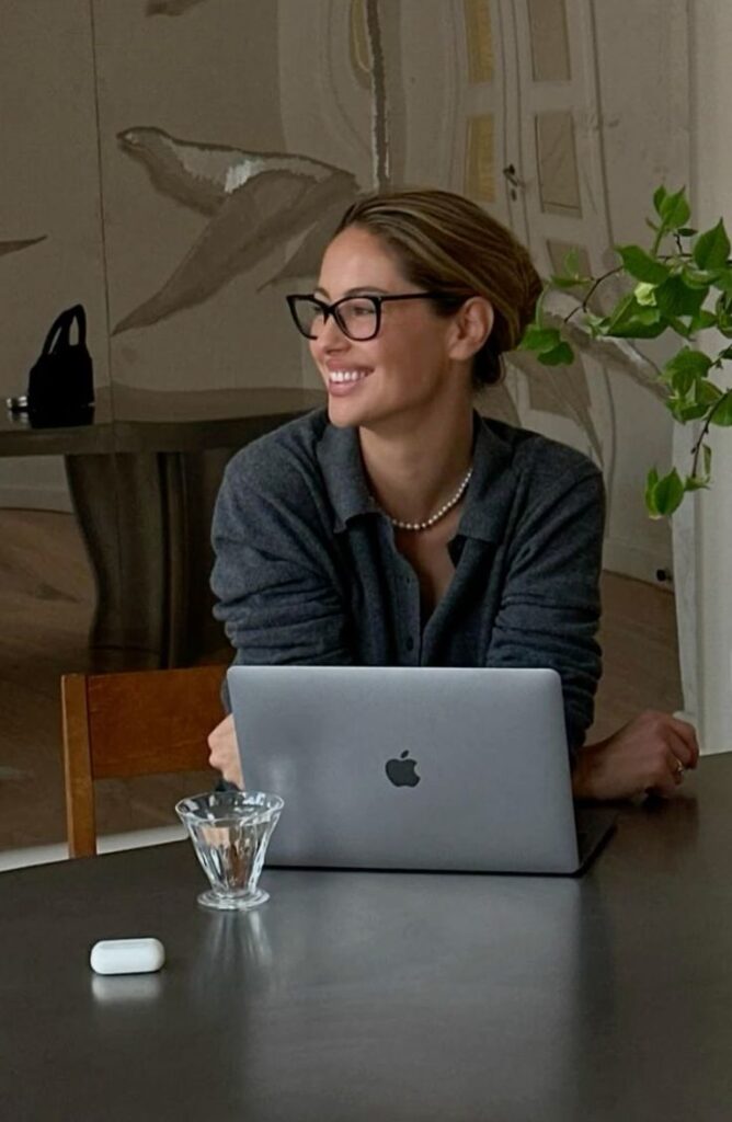 ac6d17f797bd55948530ba60102f95bb Smiling woman with glasses working on a laptop at a modern workspace, with a plant in the background. | Sky Rye Design Smiling woman with glasses working on a laptop at a modern workspace, with a plant in the background.