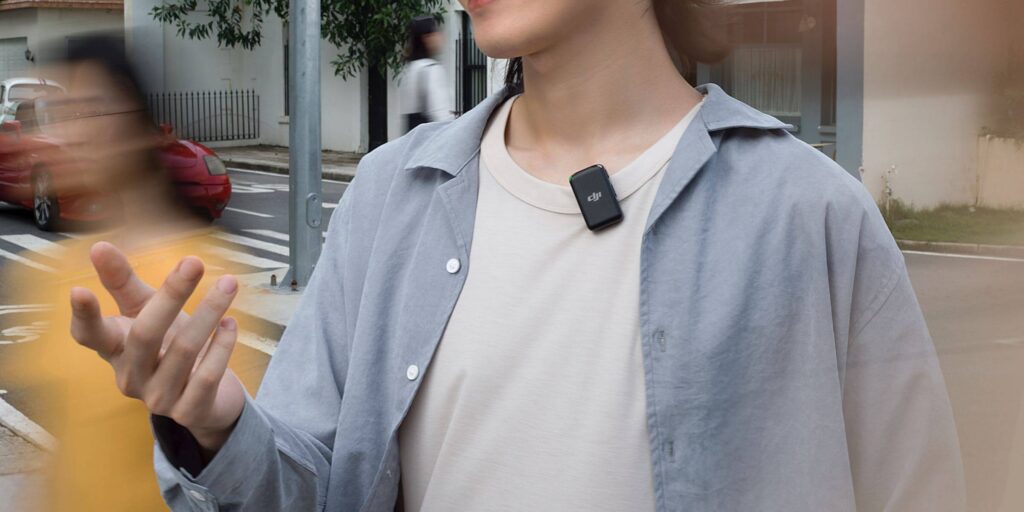 Person in street wearing blue shirt and DJI microphone, with blurred motion in the background.