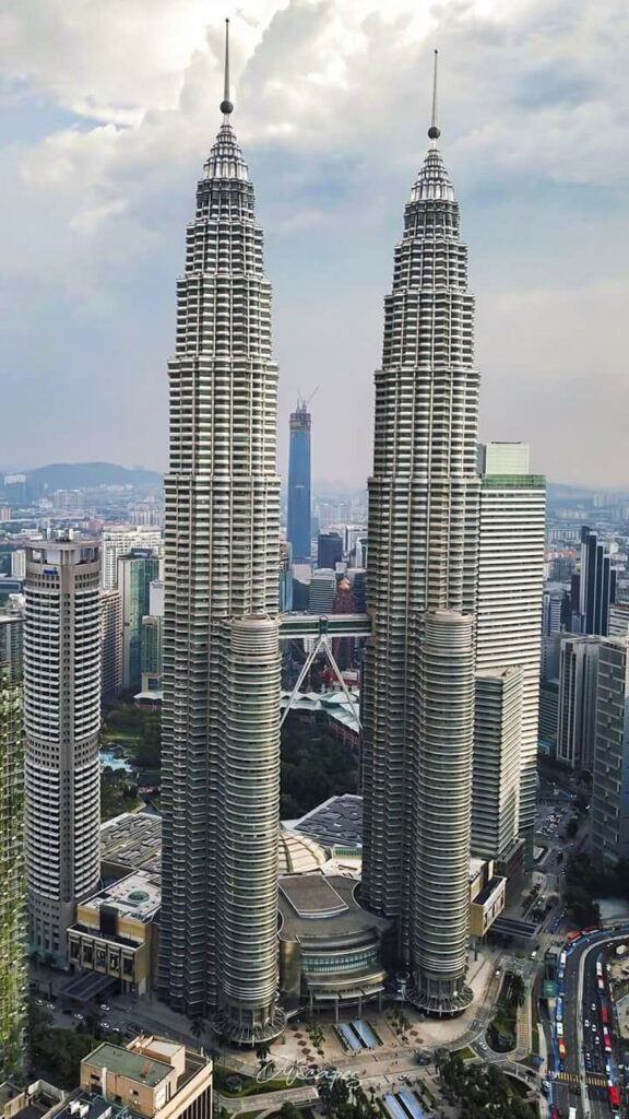 Twin towers against city skyline under cloudy sky, featuring modern architecture and urban development.