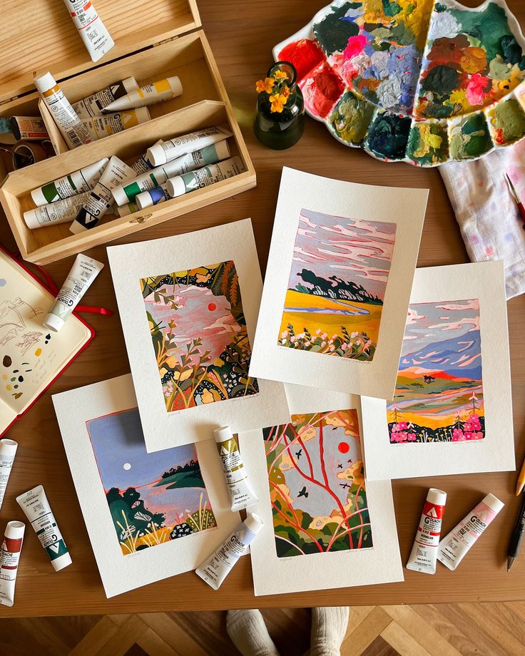 Colorful landscape art prints on table with paint tubes and palette, showcasing artistic creativity and painting supplies.