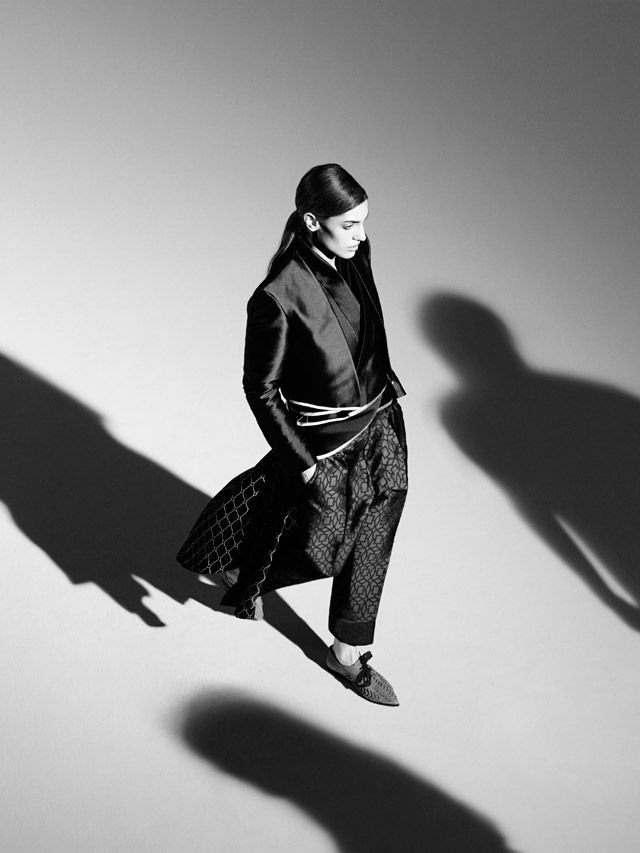 Fashion model in stylish black-and-white outfit with dramatic shadows, walking confidently on a runway.