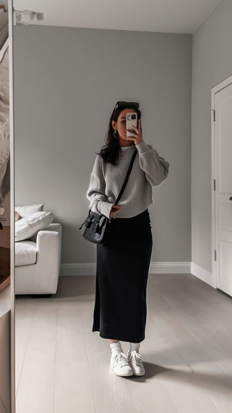 Woman in cozy sweater and skirt takes a mirror selfie, showcasing casual autumn fashion with a black bag and white sneakers.